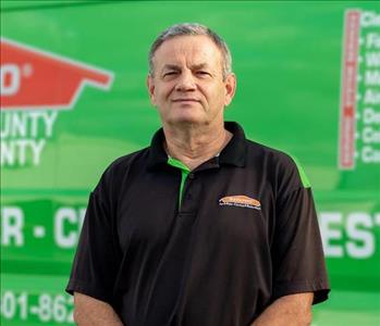 A SERVPRO male crew member wearing black polo. Green background.